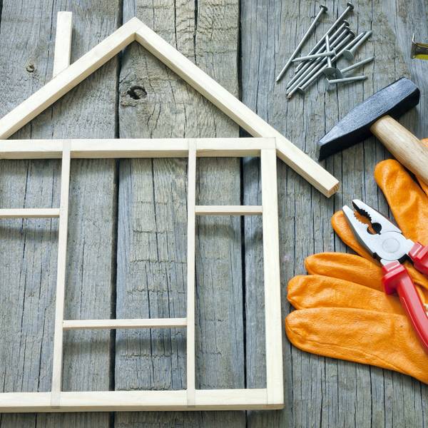 ein kleines Modell von einem Haus aus Holz, daneben Handschuhe, eine Zange und ein Hammer