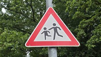Straßenschild "Achtung Schulkinder" an einem Mast. Im Hintergrund sind grüne Baumblätter.