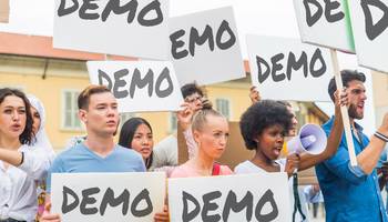 Demonstranten halten Schilder mit der Aufschrift „Demo“ nach oben.